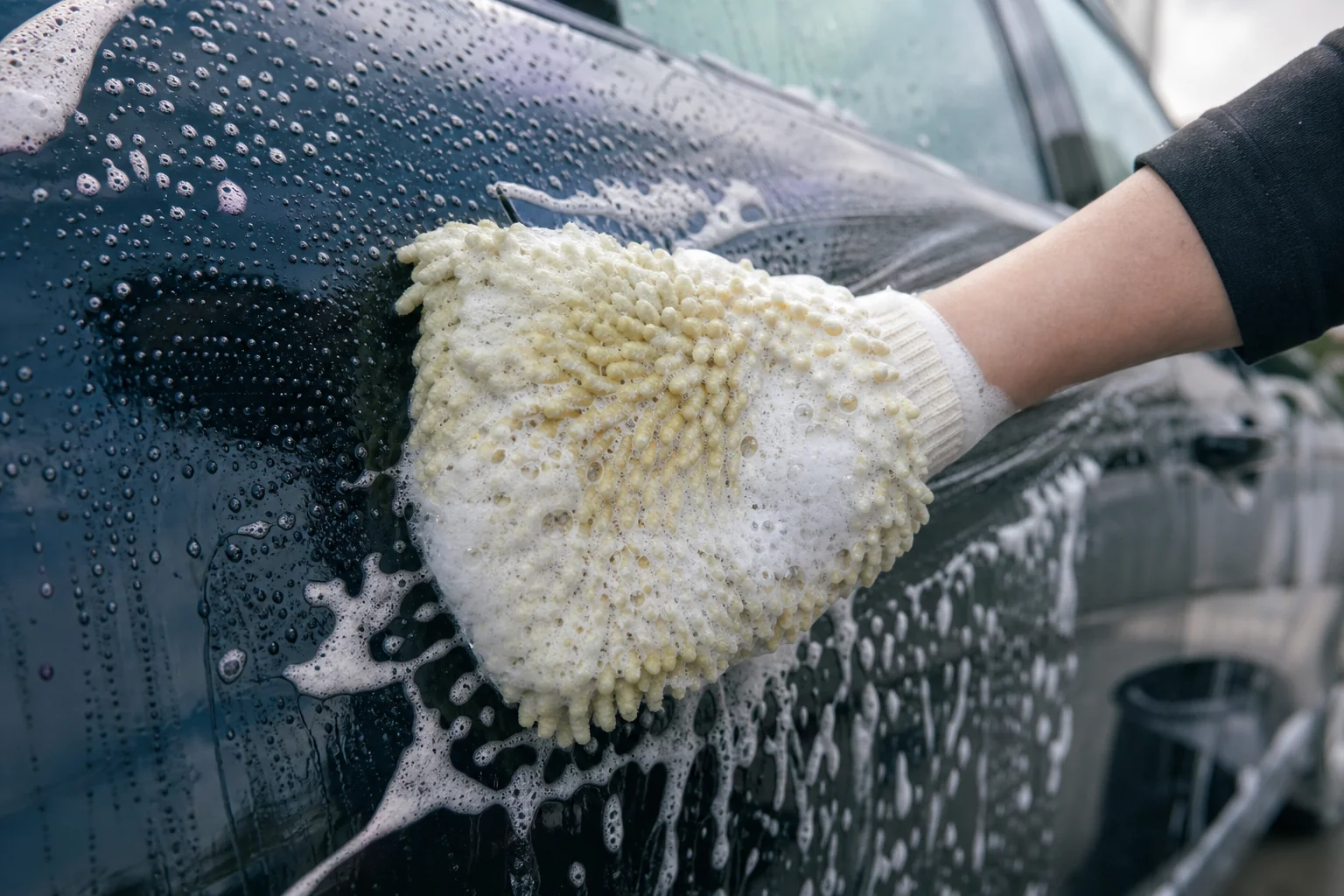 車のドアを泡をのせた洗車用ミットで一方向にすべらせるように洗っている手元